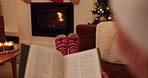 Person, book and reading in living room for story, fiction novel and knowledge at home. Feet, socks and comfortable on sofa with fireplace for literature, hobby and relax to enjoy Christmas break