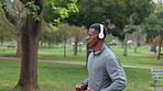 Running, headphones and black man with fatigue in nature for cardio, wellness or outdoor fitness in morning. Tired, athlete and runner with music in park for training playlist, sport or workout break