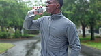 Workout, break and black man drinking water in nature for training, refreshment and fitness hydration. Athlete, tired and runner with bottle of h2o in park for sports recovery, exercise and nutrition