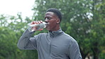 Training, break and black man drinking water in nature for workout, refreshment and fitness hydration. Runner, tired and athlete with bottle of h2o in park for sports recovery, exercise and nutrition
