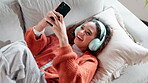 Music, phone and streaming with woman on sofa in living room of home for audio or radio from above. Headphones, funny and laughing with happy person listening to sound in apartment for break or rest