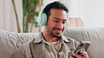 Home, smartphone and man on sofa, headphones and live stream with music. sound and smile. Person, apartment and guy with cellphone, headset and mobile user with song, audio and connection with app