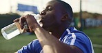 Sports, soccer and black man with water for drinking, hydration and wellness after training for game. Football field, male person and player on break with h2o liquid, practice and beverage for thirst