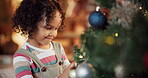 Happy kid, girl and decorate on Christmas tree for festive, holiday and celebration in home. Female person, toddler and playful with ornament, lights and living room for event on vacation in December