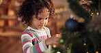 Happy kid, girl and ornament on Christmas tree for festive, holiday and celebration in home. Female person, toddler and playful with decorate, lights and living room for event on vacation in December