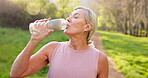 Mature woman, water and nature for fitness, drink and hydration with break, electrolytes and health. Female person, bottle and thirsty outdoor for exercise, workout and retirement with morning run