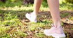 Woman, legs or walking with shoes in forest for hiking, journey or exercise in nature. Closeup, female person or feet with sneaker on grass field for travel adventure or stroll in wilderness or woods