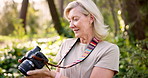 Senior woman, photographer and hiker with camera in forest or woods for sightseeing or tourism. Mature, female person or traveler with technology or lens for picture, photography or memory in nature