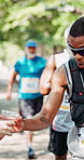 Running, water and black man in marathon in nature with group for outdoor exercise, competition or fitness. Sports, energy and African athlete with hydration drink for cardio workout in race in park.