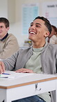 Education, laughing and student man at desk in classroom for lecture, lesson or study. Funny, humor and smile of funny learner at college, school or university for growth, learning and development