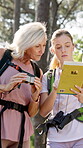 Mother, hike and woman with book in forest for bird watching, location or manual on adventure. Daughter, binoculars and mature parent with travel guide in nature for holiday, information or exploring