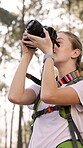 Woman, hiker and photography with camera in forest for sightseeing, tourism or nature hobby. Photographer, person or traveler with lens for picture, memory or photoshoot in woods with technology