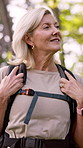 Happy, mature woman and hiking with backpack in forest for adventure, travel or outdoor journey. Female person, hiker or tourist with equipment or bag for trekking or sightseeing in nature or woods