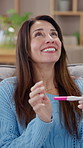 Woman, home and happy with pregnancy test with good news or positive results in living room. Female person, maternity and smile or excited with testing stick on couch for family planning or fertility