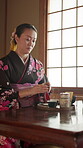 Mature woman, tea and kimono in Japan for serving, traditional drink and cultural hospitality in home. Japanese person, cup and matcha in living room for offer, detox beverage or preparation at table