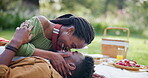 Smile, black couple and kiss for picnic on grass with romantic date, love and food basket of anniversary. Happy, people and laughing with comic affection, relationship bonding and commitment outdoor