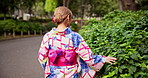 Asian woman, walking and back with kimono in nature for travel, journey or natural sustainability. Japanese, female person or culture with fashion, leaves or bushes for commute at park or garden