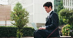 Business man, laptop and park bench in city, thinking and reading for remote work, typing and project. Person, computer and journalist in nature for review, feedback and check email by trees in Japan