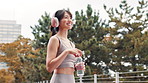 Park, smile and woman with headphones, water and hydration for runner, outdoor and wellness. Morning, streaming and Japanese person with music for exercise, thirsty and athlete with bottle in Japan