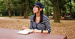 Woman, eating and park with food, gen z and picnic bench in Japanese forest with travel and college student break. Outdoor, takeaway and calm in autumn and Japan on weekend with meal to relax
