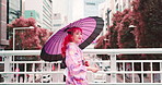 Woman, kimono and walking with umbrella in urban, outdoor bridge and travel for sightseeing. Female person, traditional clothes and weekend in town for culture, local fashion and exploring Japan