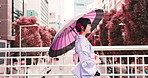 Woman, holiday and walking with umbrella of Japan, outdoor bridge and travel to city for view. Female person, traditional clothes and relax in town for culture, local fashion and exploring urban