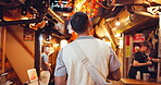 Walking, market and back of man with travel on weekend trip, adventure or holiday in city. Journey, exploring and male person with tourism at night retail bazaar on vacation in Japanese town.