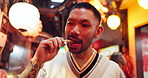 Asian man, street food and eating at night for travel, tourism and holiday outdoor in Japan. Japanese person, city and enjoy snack, squid and hungry for meat at market on vacation, adventure and trip