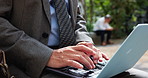 Businessman, hands and typing on laptop outdoor for case review, legal administration or writing report. Headphones, lawyer or law research at city park for client policy update or listening to music