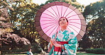 Woman, kimono and walking with umbrella in park, outdoor bridge and travel to woods for thinking. Female person, traditional clothes and relax in nature for culture, local fashion and explore Japan