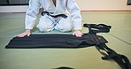 Person, hands or clothing with outfit for martial arts, fashion or folding aikido gi on floor in dojo. Japan, closeup or black belt fighter with material, fabric or tradition uniform for self defense