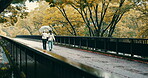 Walking, raining and friends with umbrella, city and bonding of people with waterproof, back and journey. Outdoor, bridge and tourism of location, weather and travel with  tourists, holiday and Japan