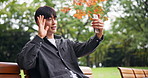 Happy, asian man and video call with wave or phone on park bench for communication or conversation in nature. Japanese, male person or tourist with smile for virtual discussion, online chat or app