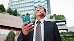 Mature businessman, smartphone and travel in street with texting, notification and low angle on commute in city. Person, phone and click on mobile app, search and direction on urban sidewalk in Japan