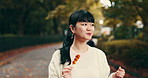 Street food, eating and walking with Japanese woman in park for dessert, traditional cuisine and holiday. Dango, taste and festival season with asian person and culture snack for sweets and lunch