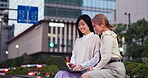 City, laptop and night with business women outdoor together for collaboration or research. Computer, conversation and smile of Japanese employee with colleague in urban town for graphic design