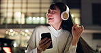 Woman, headphones and dancing at night in town, phone and streaming online for playlist. Female person, energy and outdoor music for peace in Japan, song subscription and internet for sound in city