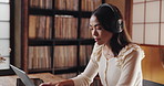 Woman, laptop and headphones for remote work in home office, typing article and listening to music. Female person, news journalist and employee online for research in Japan, podcast and hearing audio