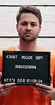 Face, man and criminal mugshot at police station with identity frame, investigation and legal photography. Male prisoner, flashlight and billboard of public safety, crime violations and inmate number