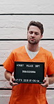 Face, man and mugshot with sign at police station of identity frame, investigation and legal photography. Male prisoner, flashlight and billboard of public safety, violations arrest and inmate number