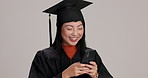 Typing, graduation and woman with phone in studio for networking, browsing or communication. Happy, cellphone and Japanese female student with contact on social media app or online by gray background