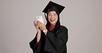 Piggy bank, happy and face of graduate in studio with money saving, investment or tuition fees. Smile, funds and portrait of Japanese woman student with cash growth for graduation by gray background.