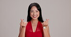 Woman, face and finger hearts in studio with smile, fashion and expression for care. Japanese person, happy and love emoji on gray background for like icon, trendy style and Valentines day symbol