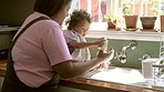 Cleaning, washing dishes and mother with kid in kitchen for learning, child development and chores. Family home, housework and mom bonding with baby by sink with plates, soap and sponge for hygiene