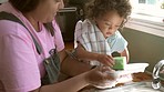 Help, washing dishes and mother cleaning with child in kitchen for learning, child development and chores. Family home, housework and mom with baby by sink with plates, soap and sponge for hygiene