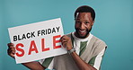 Happy, black man and billboard with sale for deal, promotion or advertising on a blue studio background. Portrait, male person or promoter with smile for shopping announcement, alert or notification