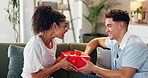 Couple, love and gift on sofa for Valentines day, celebration or romantic gesture in home. Shocked woman, man or box in lounge with birthday surprise, present or relationship milestone with thank you