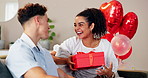 Couple, love and gift on home for celebration, Valentines day and romantic gesture on sofa. Shocked woman, man or box in lounge with birthday surprise, present or relationship milestone with balloons