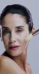 Makeup, brushes and face of woman in studio on gray background for wellness, skincare and beauty. Cosmetology, application and portrait of mature person with tools for cosmetics, powder and products