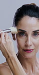 Makeup, brushes and face of mature woman in studio on gray background for wellness, skincare and beauty. Cosmetology, application and portrait of person with tools for cosmetics, powder and products